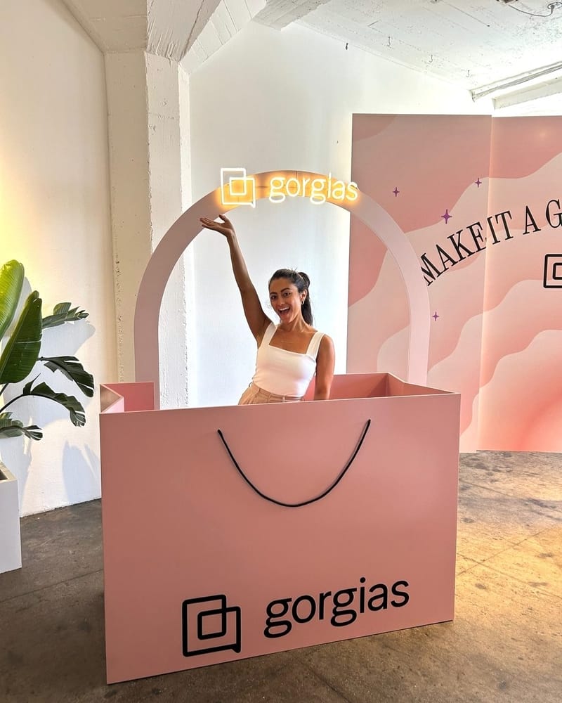 A guest waving from inside a giant pink Gorgias shopping bag under a lit Gorgias sign
