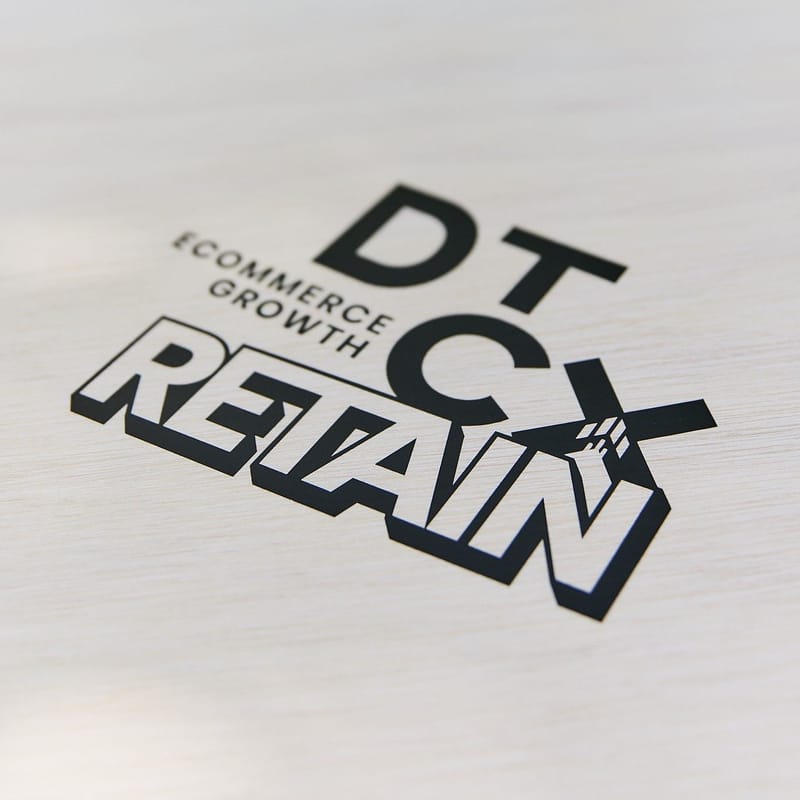 Close view of the DT CX Ecommerce Growth Retain logo printed on a pale surface