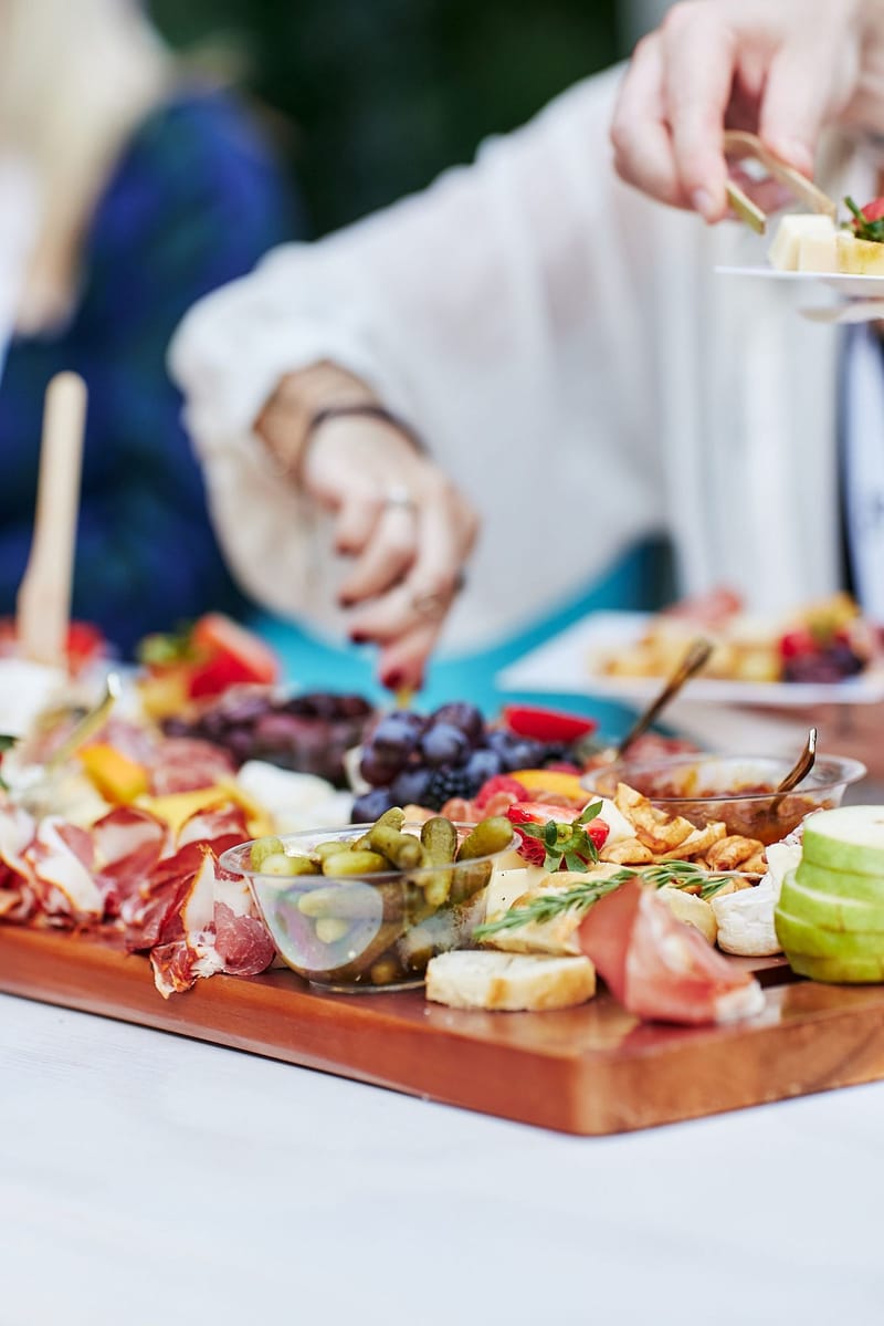 Hands reaching for a charcuterie board of cured meats, cheese, olives and grapes