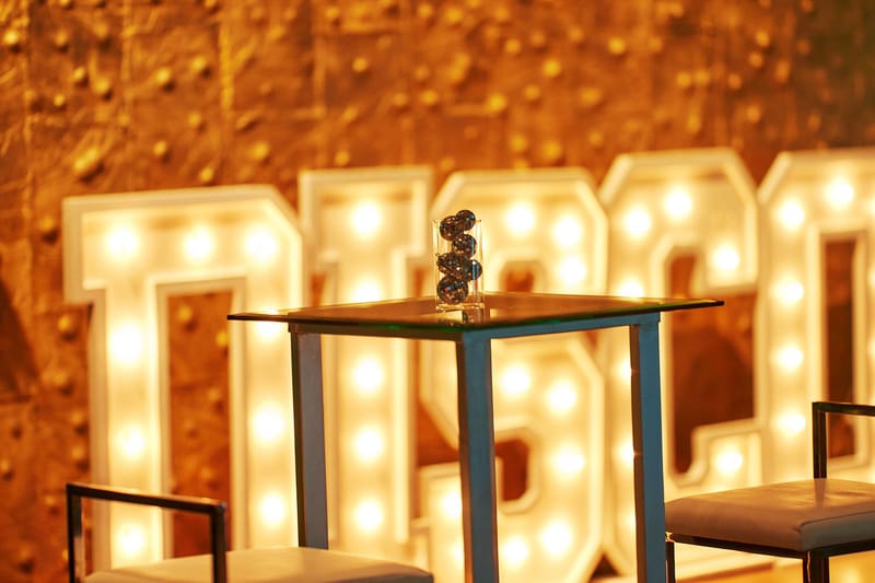 Lit marquee letters spelling DISCO behind a small high-top table