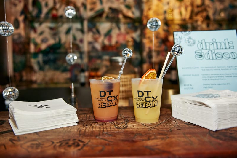 Close view of two orange drinks in DTCx Retain cups with dried citrus and disco ball stirrers