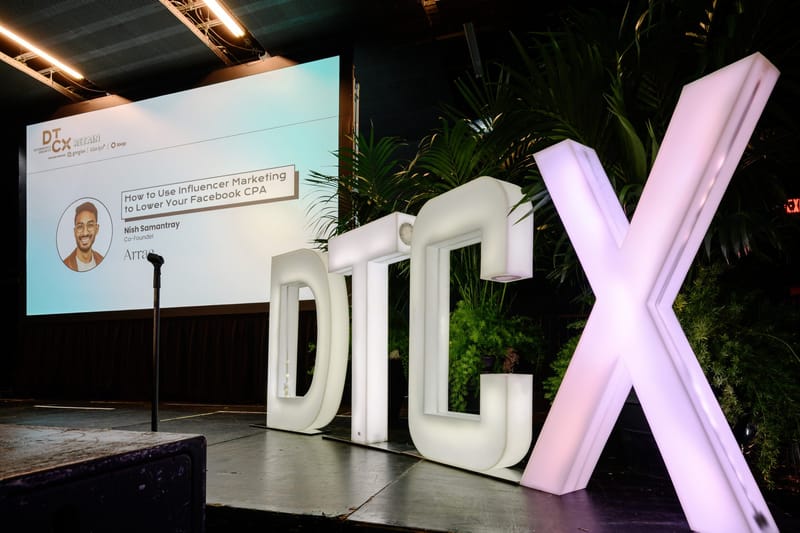 Giant lit DTCX letters beside a screen showing a talk on influencer marketing