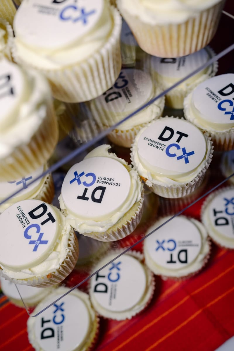 Cupcakes topped with DT CX Ecommerce Growth logos on a red cloth