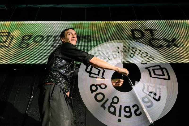 Performer in a sequined top holding a large lit disc printed with the gorgias logo
