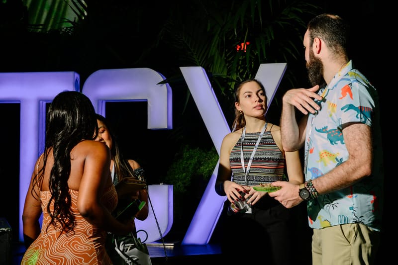 Three guests talking in front of glowing purple DTCX letters