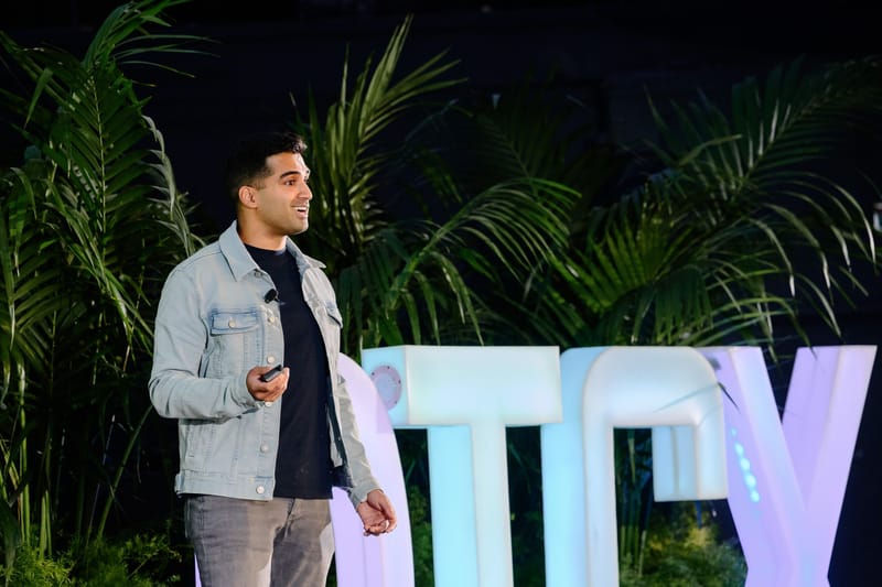Speaker in a denim jacket presenting in front of lit DTCX letters and palms