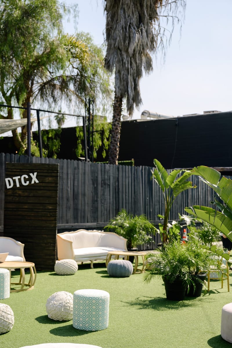 Turf patio with a black DTCX sign, a white sofa, poufs and potted plants