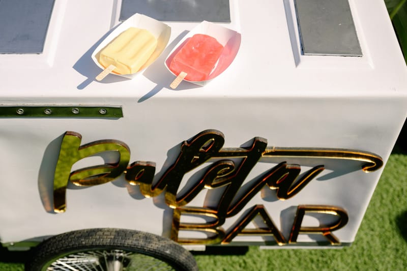 Paleta Bar cart with gold lettering and two popsicles on top, on artificial turf