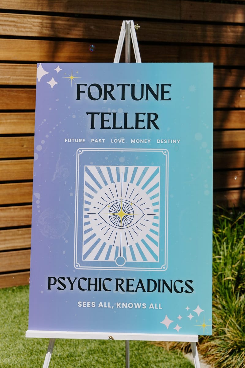 Fortune Teller Psychic Readings sign reading Sees all, knows all on an easel by a wooden fence