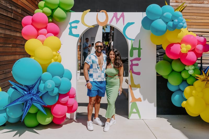 Man and woman posing in the ECOMCHELLA arched entrance surrounded by colorful balloon garlands