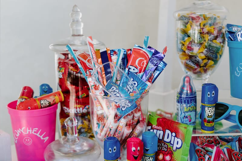 Pink ECOMCHELLA cup of Push Pops beside a glass jar of Razzles, Fun Dip, Skittles and Ring Pops