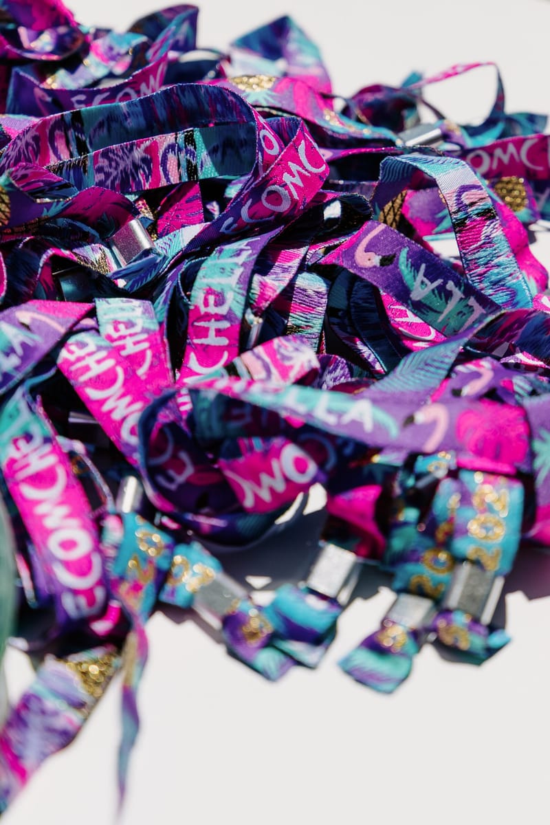 Pile of woven festival wristbands printed ECOMCHELLA in pink, purple and teal