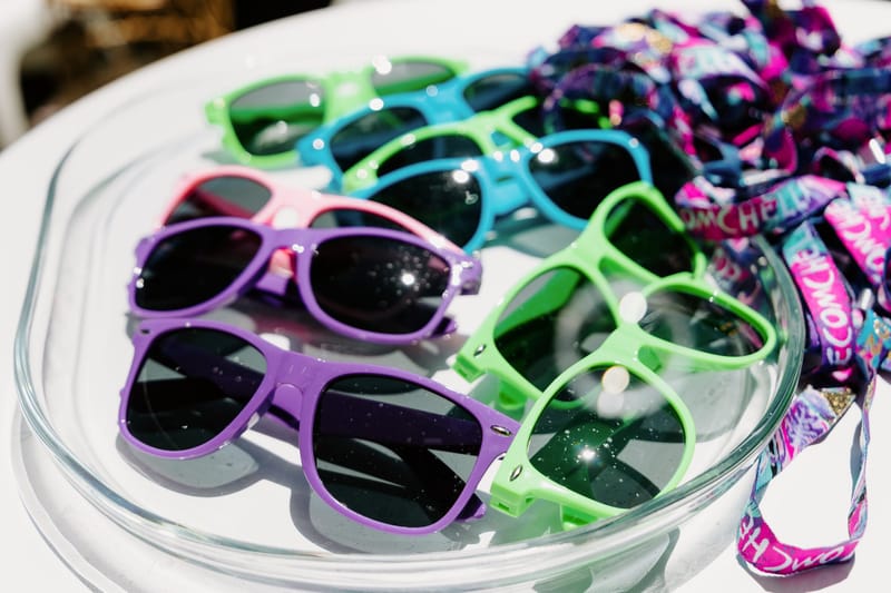 Clear tray of green, purple and pink sunglasses beside a pile of ECOMCHELLA wristbands