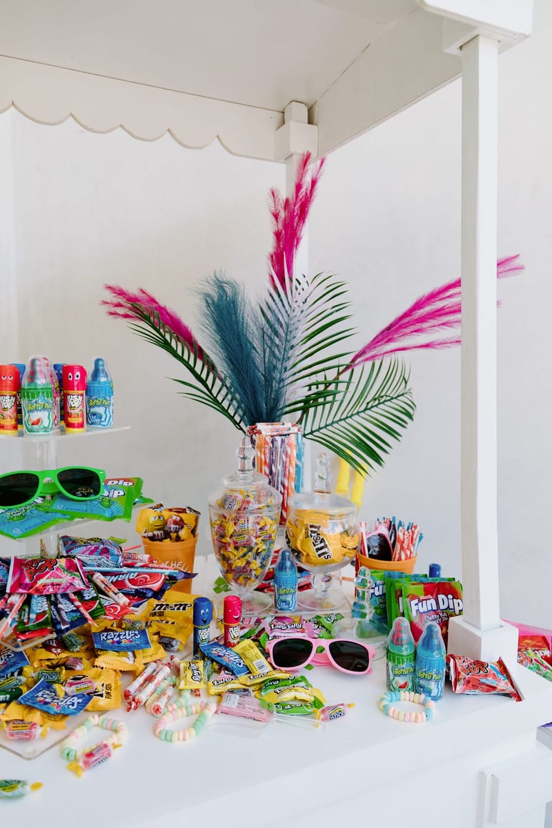 White candy cart with palm leaves, candy jars, Fun Dip, Baby Bottle Pops and sunglasses spread out
