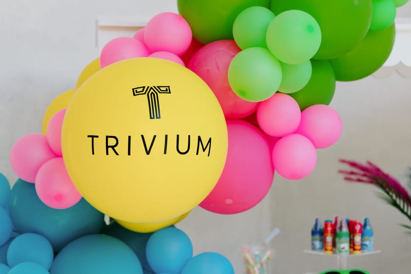 Yellow TRIVIUM logo balloon set in a pink, green and teal balloon garland