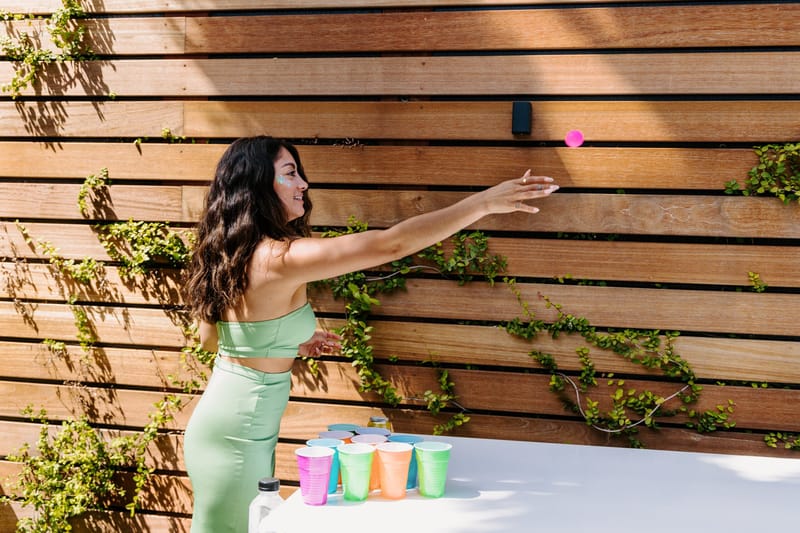 Guest tossing a ping pong ball toward colorful cups in front of a slatted wooden fence