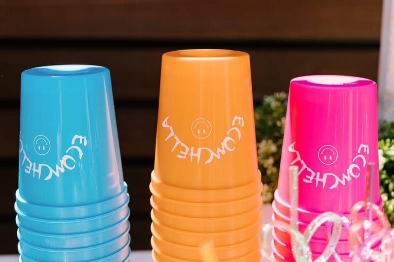 Stacks of blue, orange and pink cups printed ECOMCHELLA with smiley faces