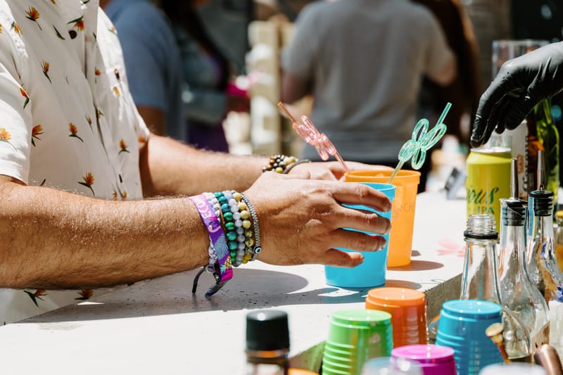 Guest wearing beaded bracelets and a festival wristband holding a blue cup at the bar