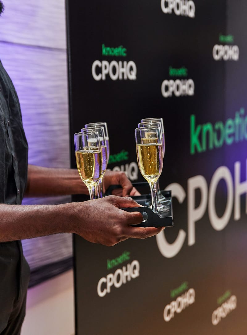 Server holding a tray of champagne flutes in front of a knoetic CPOHQ backdrop