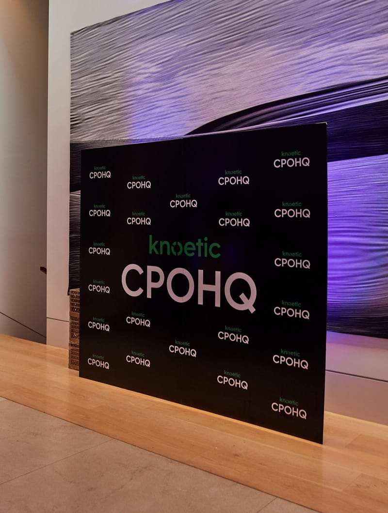 Black knoetic CPOHQ logo backdrop in a room with purple uplighting
