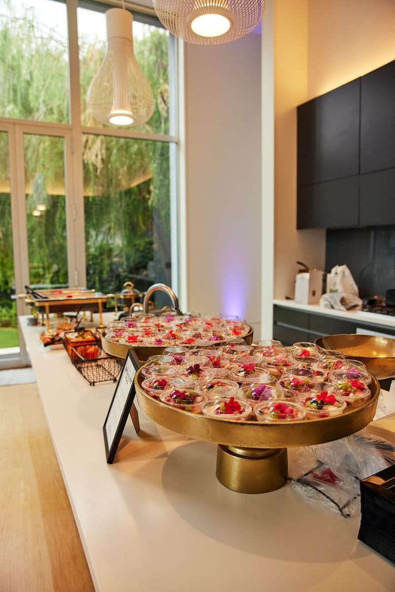 Kitchen counter with gold stands of small cups topped with red flowers beside tall windows
