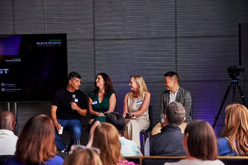 Four panelists with microphones in front of a CPOHQ Elevate 2024 screen and a seated audience