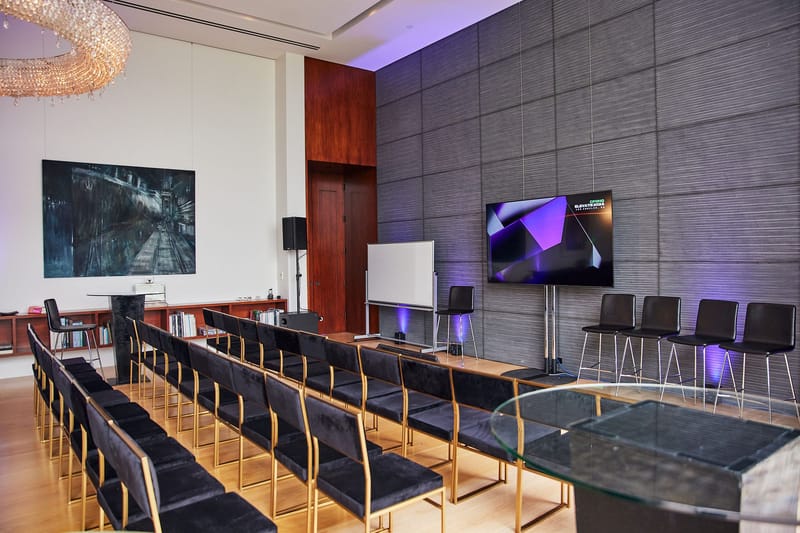 Rows of black chairs facing a wall screen in a room with purple uplights