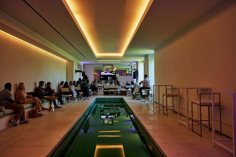 Long room with a narrow reflecting pool, bar stools and guests seated along the wall