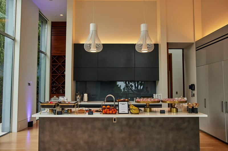 Kitchen island laid with food under two white pendant lights in a tall room