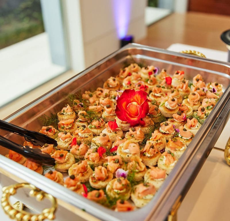 Chafing dish of canapés topped with dill and edible flowers, with a red rose in the center