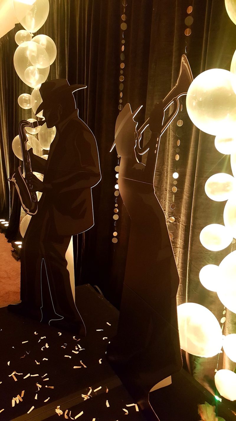 Silhouette cutouts of a saxophone player and a trumpet player against velvet drapes and strands of gold discs