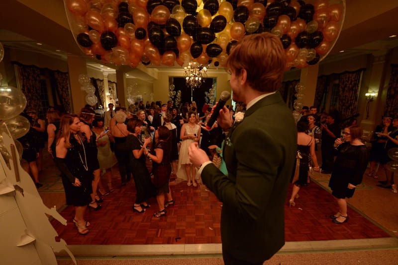 Guests dancing on a parquet dance floor under a ceiling covered in black and gold balloons