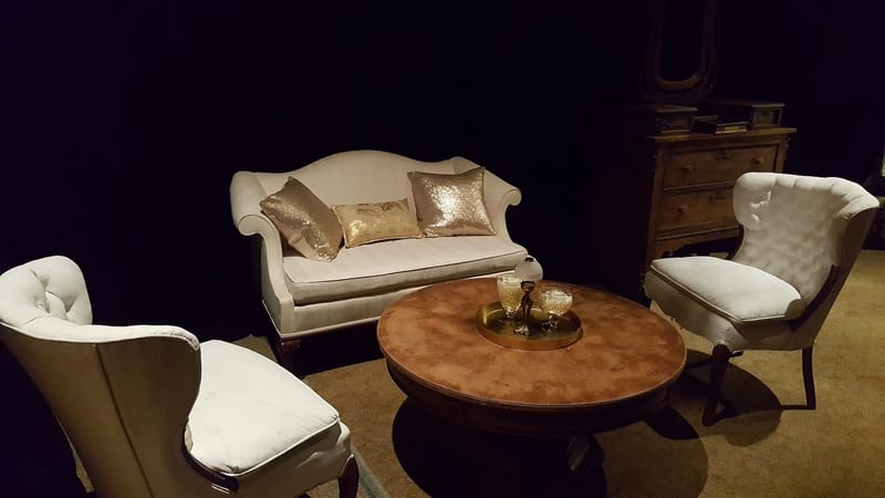 White sofa with gold sequin pillows and two white tufted armchairs around a round wooden table