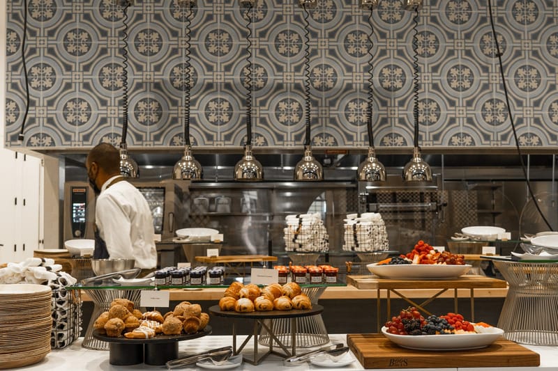 Pastry spread of chocolate croissants, coffee cake and berry platters below a patterned tile wall