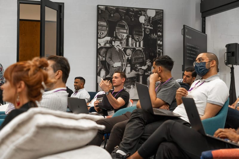 Attendees with laptops listening from teal armchairs beneath black and white framed photographs