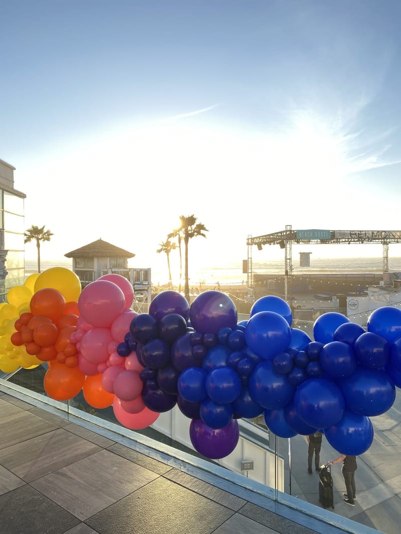 Balloon garland in yellow, orange, pink, purple and blue along a terrace railing above the beach