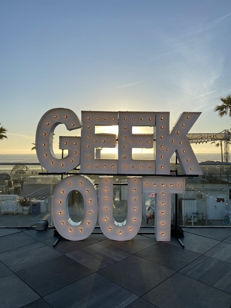 GEEK OUT marquee letters at sunset on a terrace overlooking the beach and palm trees