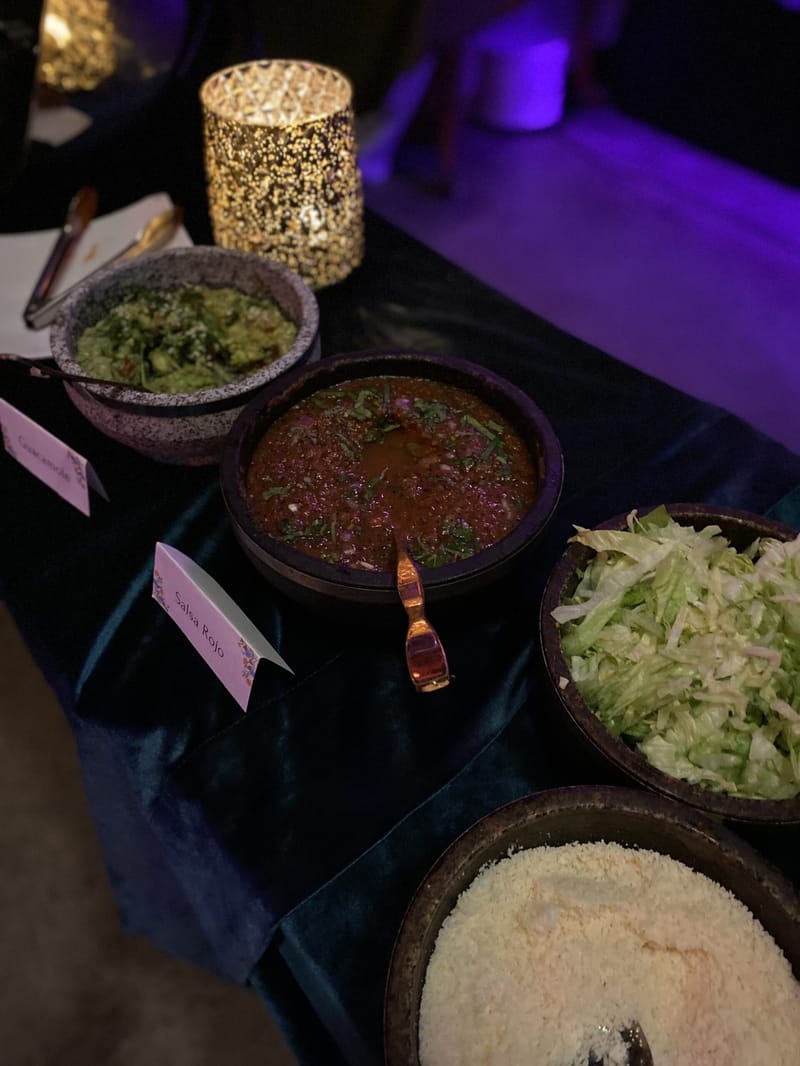 Stone bowls of guacamole, salsa rojo and shredded lettuce with name cards on a dark velvet tablecloth