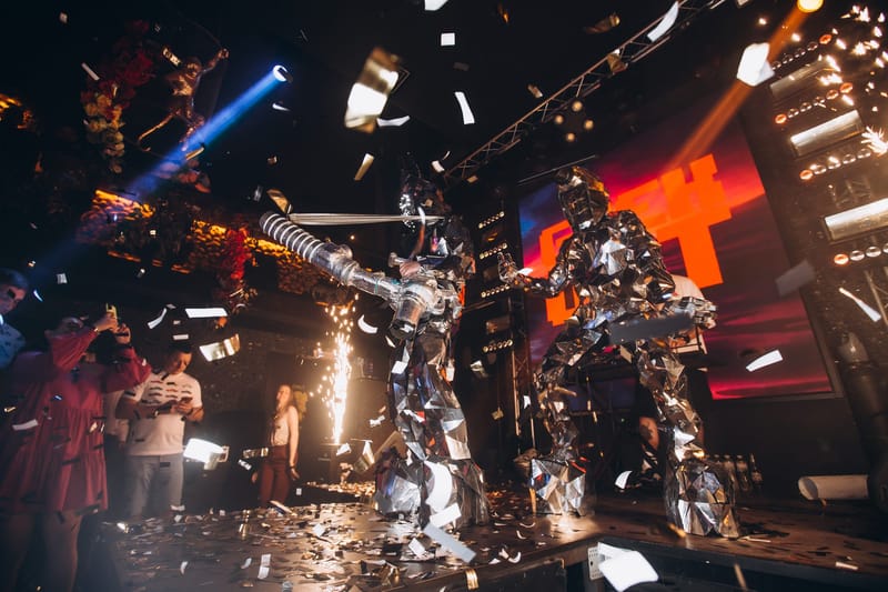 Two performers in mirrored robot suits on stage as confetti falls and sparklers fire