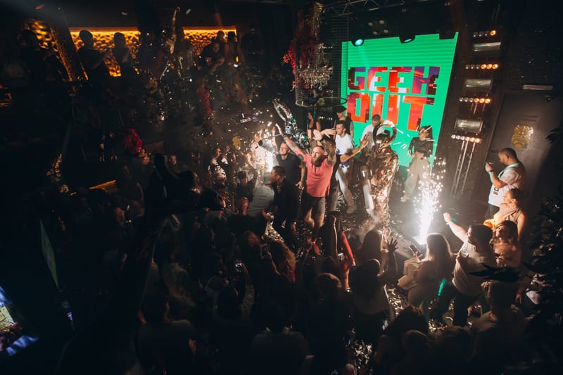 Crowd around a stage with sparklers and a performer in front of a green GEEK OUT screen