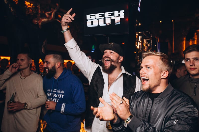 Guests cheering and clapping under a GEEK OUT screen, one in a blue GeekOut hoodie