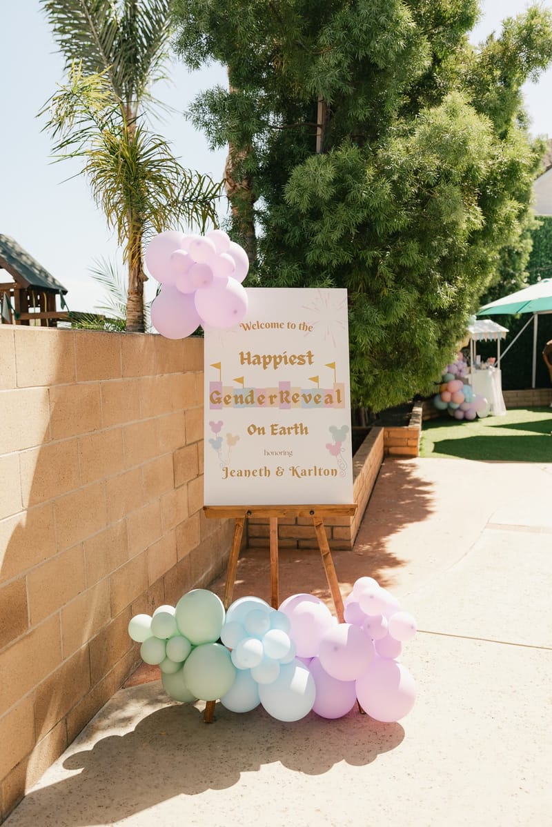 Welcome sign on an easel reading Happiest Gender Reveal on Earth featuring Jeaneth and Karlton, with pastel balloons