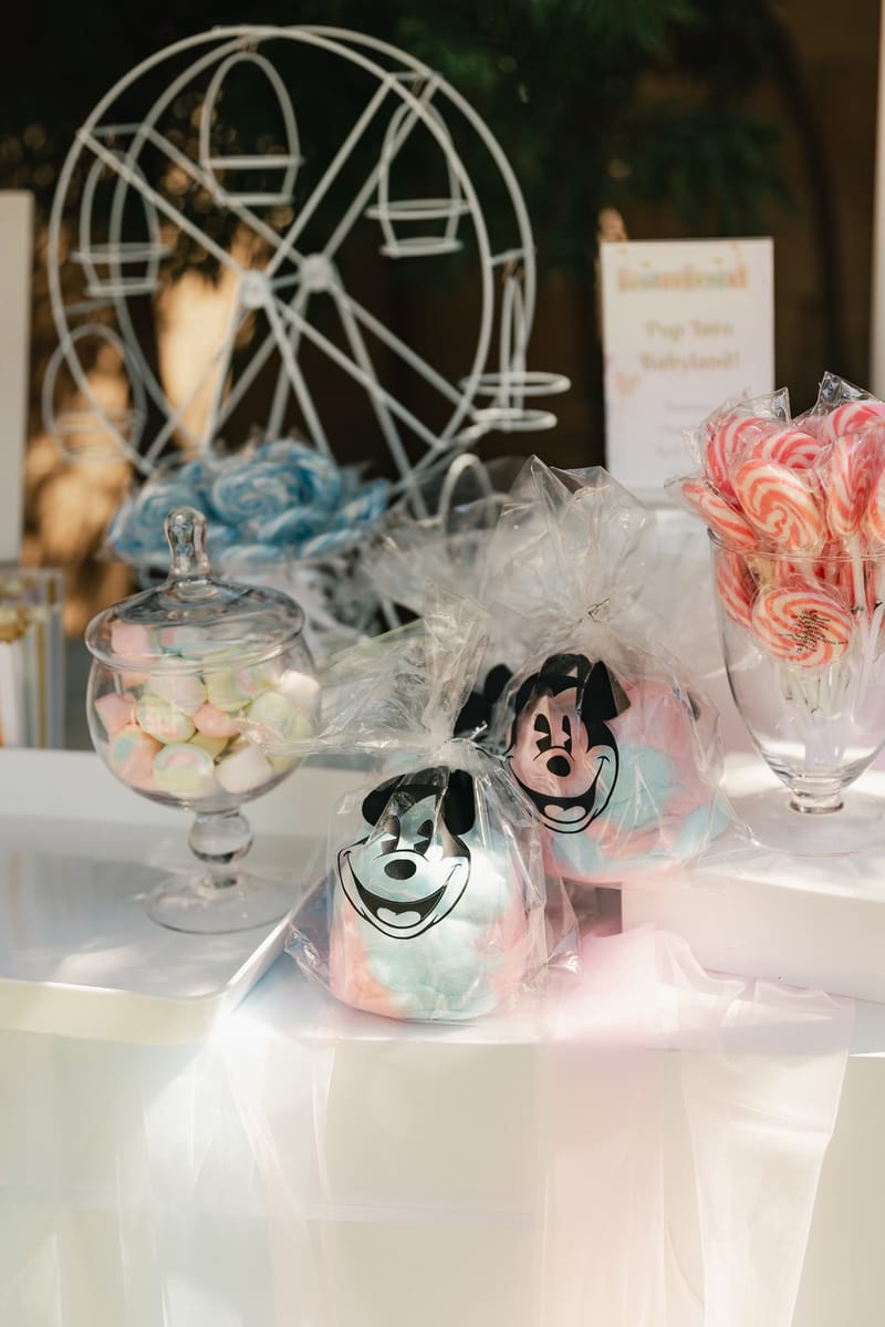 Mickey Mouse cotton candy bags and jars of sweets in front of a white Ferris wheel stand