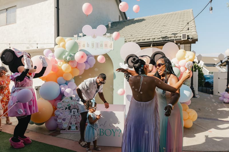 Guests cheering as pink balloons rise from the reveal box beside Minnie Mouse