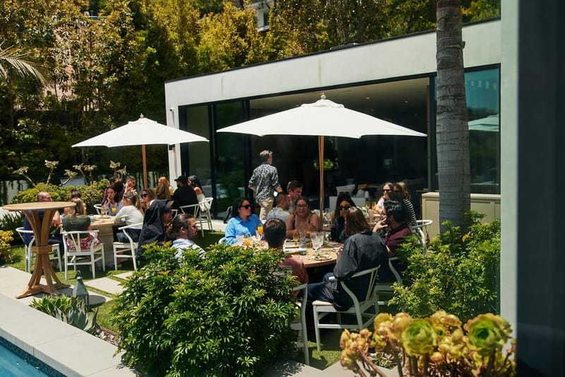 Guests eating lunch at round tables under white umbrellas beside the pool