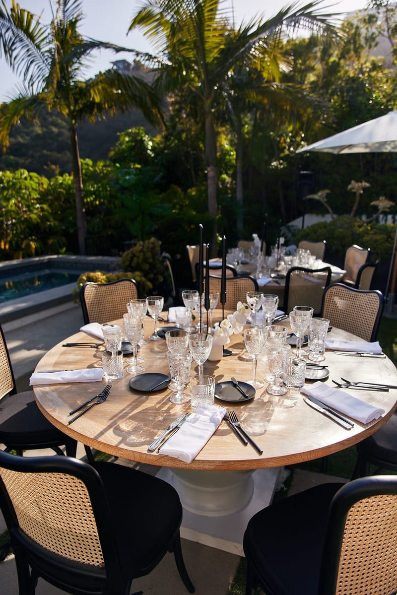 Round dinner table with cane-back chairs, crystal glasses and black taper candles on the lawn