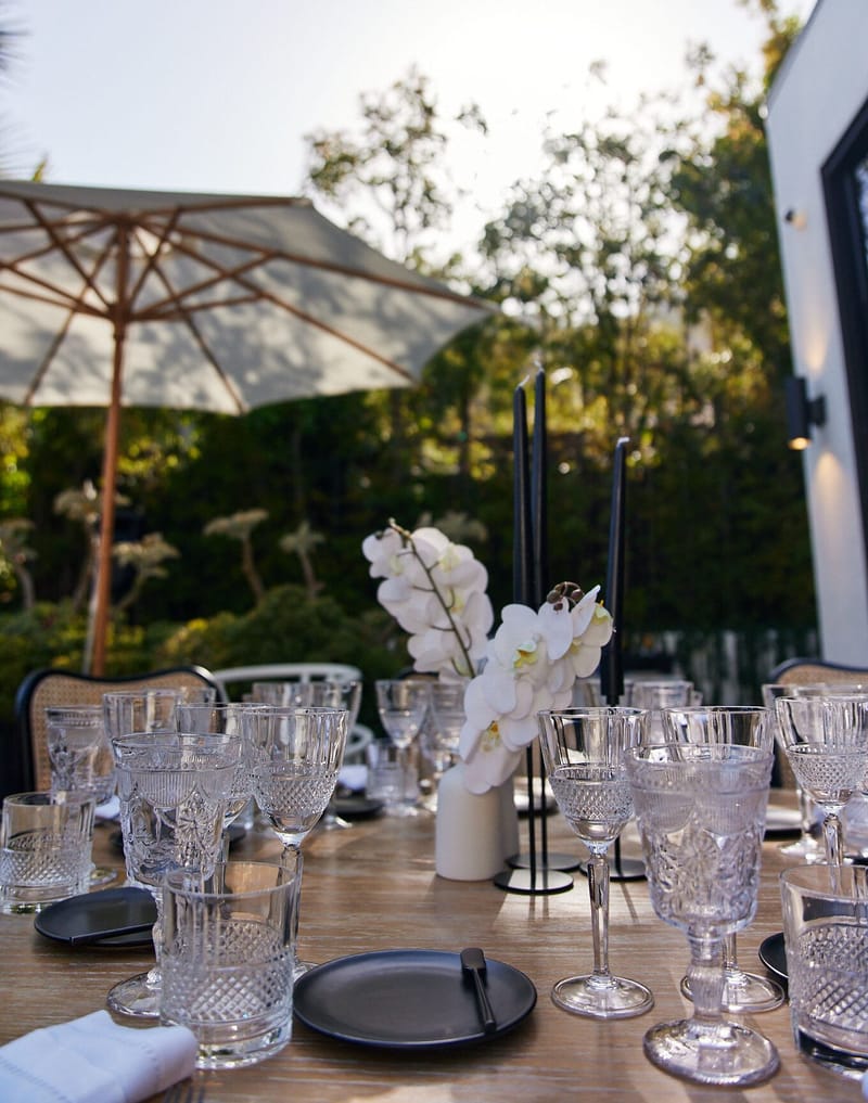 Crystal glasses, black plates and white orchids on a wooden table under a white umbrella