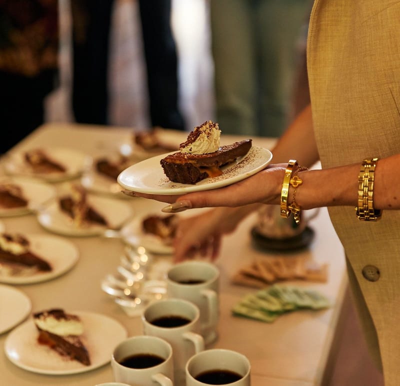 A server holding slices of chocolate cake over plates and cups of coffee