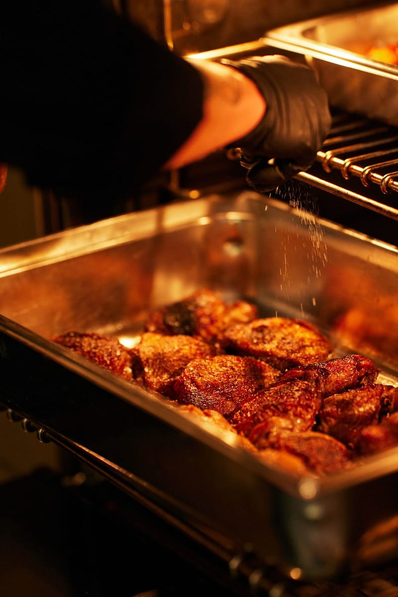 Seared meat in a chafing pan being seasoned