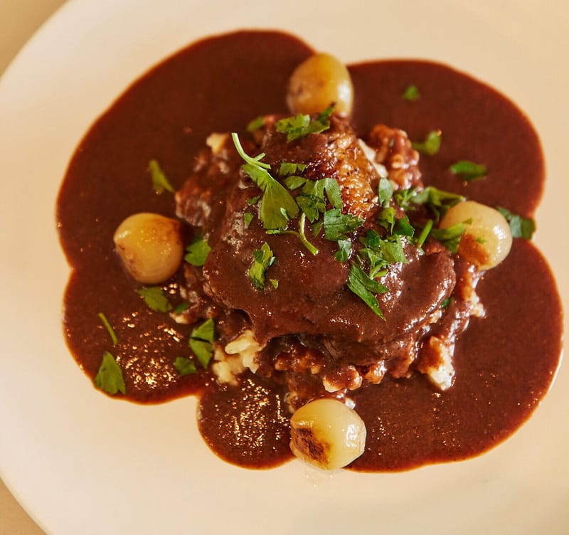 Braised meat in dark sauce with pearl onions and chopped herbs on a white plate